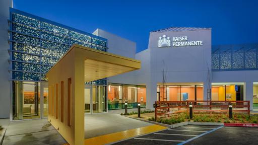 The new entry canopy, glass vestibule, fence and Laser-cut metal roof screens and glass pattern at Watsonville MOB entry as seen at night. Reception lobbies are visible within.