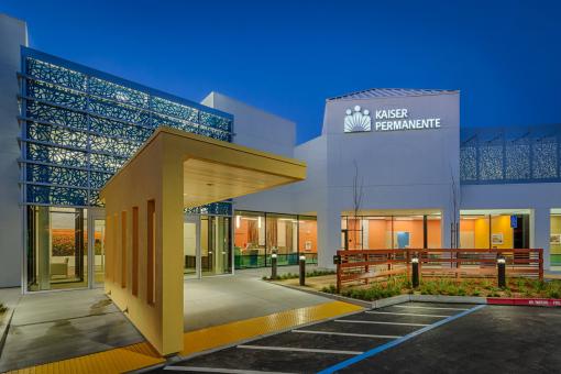 The new entry canopy, glass vestibule, fence and Laser-cut metal roof screens and glass pattern at Watsonville MOB entry as seen at night. Reception lobbies are visible within.